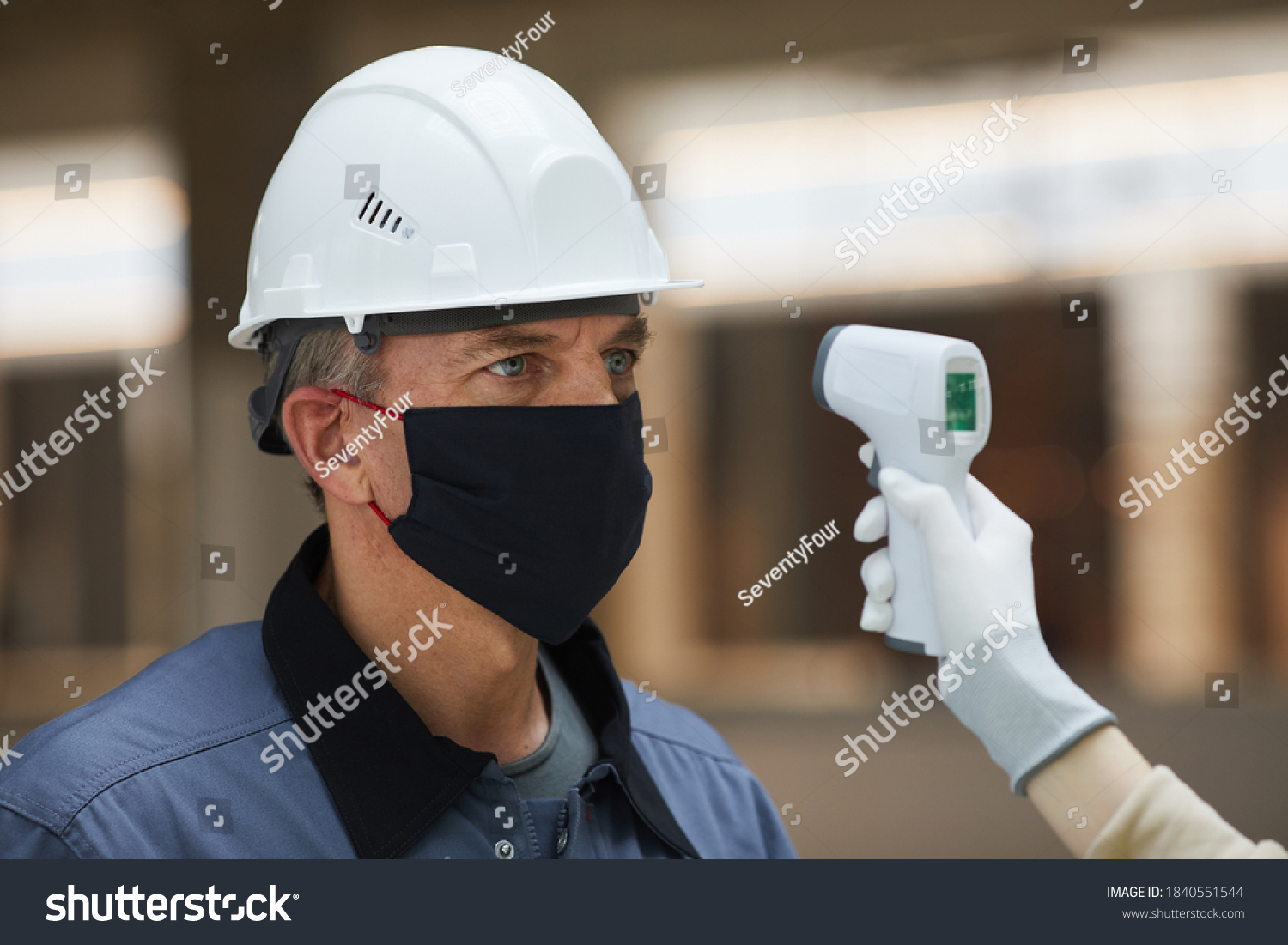 Worker in hard hat being tested for a fever with inferred thermometer