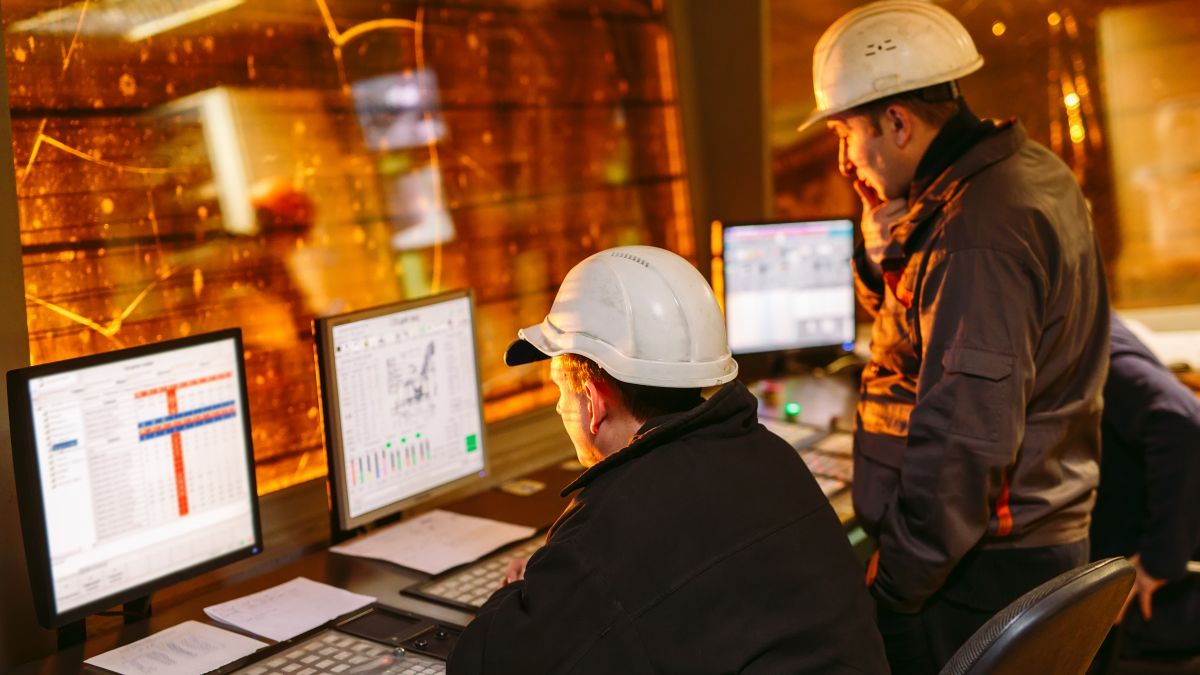 Two Dynamo engineers using computers to install substation automation. Both are wearing personal protective equipment and hard hats.