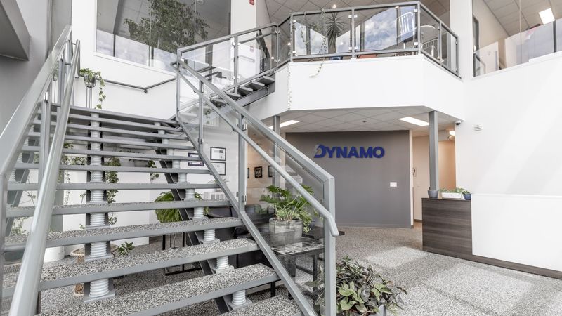 Custom-built stairs in the Dynamo front lobby located in Saskatoon, Saskatchewan. Dynamo logo on the back wall and green plants throughout.